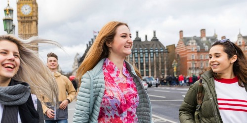 Vidám diákok London belvárosában sétálnak hűvös, borult, kicsit szeles időben, fiatalok, boldogok és rendelkeznek utasbiztosítással