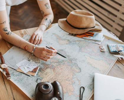 Utazási tervezés, térképen jelölő kezek, útlevél, napellenző sapka és fényképezőgép