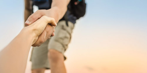 férfi segít valakinek felmászni a hegyre