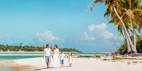 Tengerparti nyaraláson a szülők a gyerekekkel együtt élvezik a vakációt a pálmafás parton, Panoramic photo of beautiful Caucasian family on beach vacation