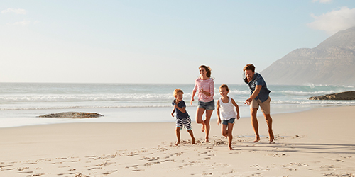 A szülők együtt futnak a gyerekekkel nyáron a tengerparti nyaraláson, családi utasbiztosítás biztonságában