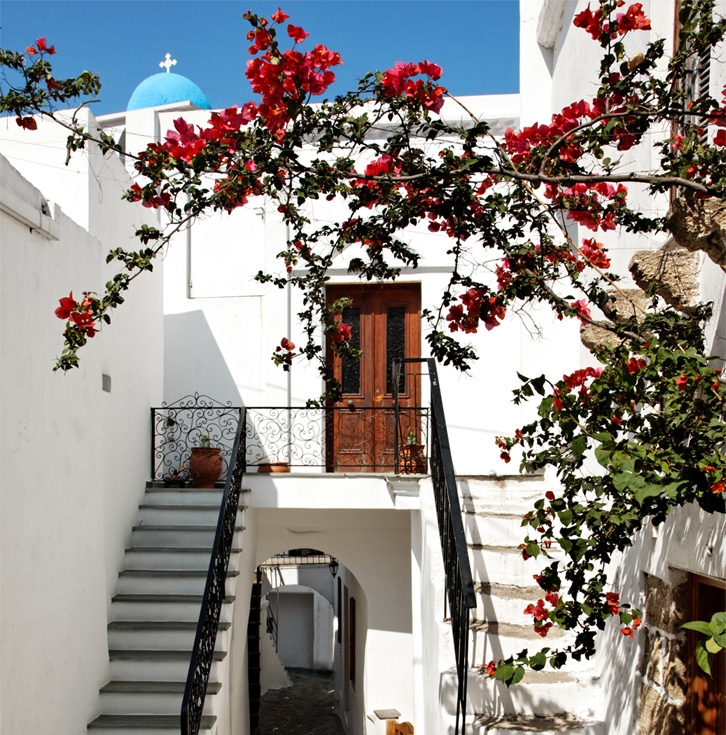 Skyros szigete Görögországban, tradicionális óvárosi sikátor és utcabejárat, virágzó fával az  előtérben, kovácsoltvas korláttal a faajtós bejárat elött