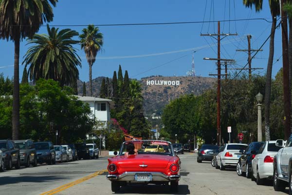 Los Angeles, USA, piros cabrio oldtimer hajt az úton, háttérben a hegyoldal Hollywood felírattal